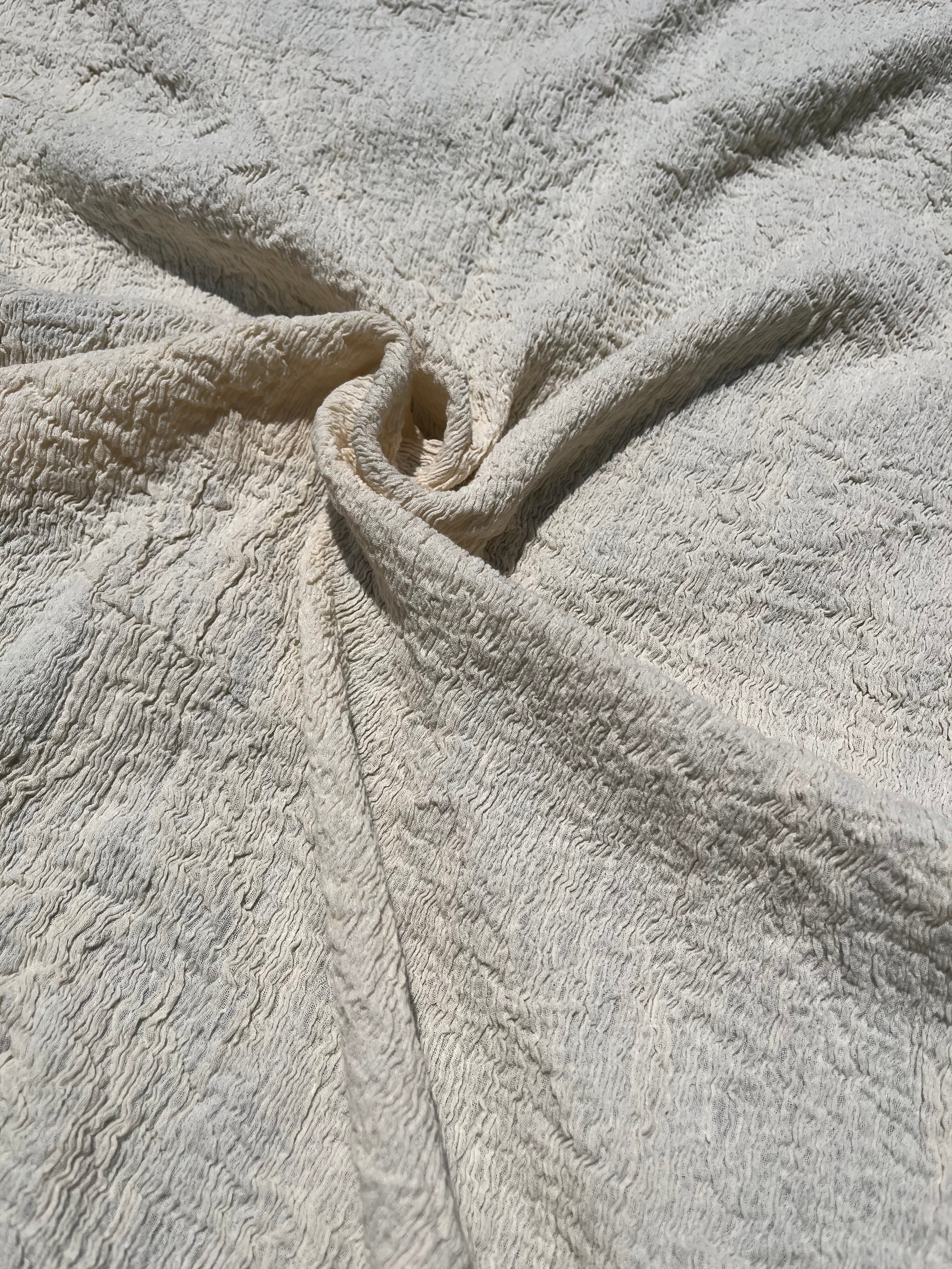 Tissu en coton froissé extensible neutre, surface texturée, coton tissé à la main blanc cassé, coton beige biologique semi-transparent et non blanchi.