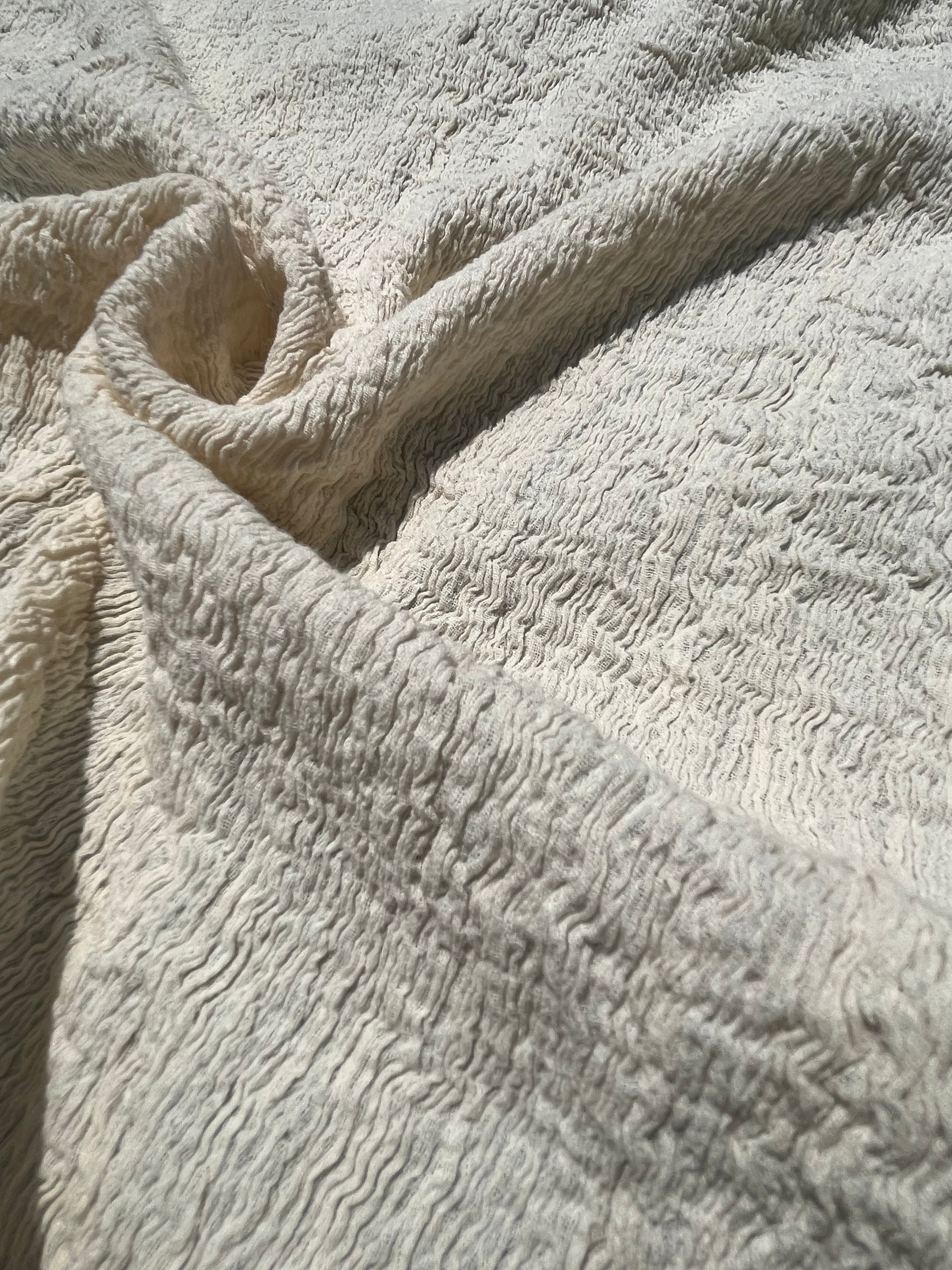 Tissu en coton froissé extensible neutre, surface texturée, coton tissé à la main blanc cassé, coton beige biologique semi-transparent et non blanchi.